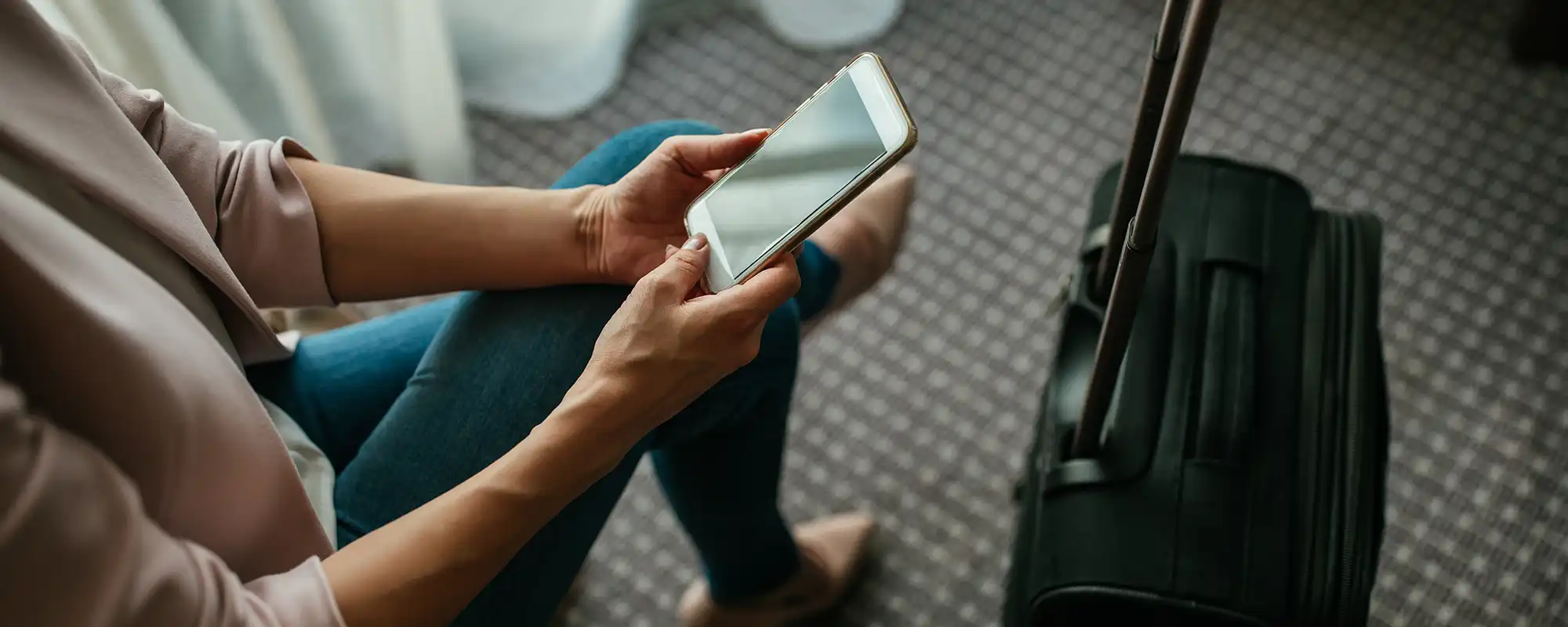 Batteries externes en avion – règles et sécurité à bord Batteries externes avion : passager utilisant un smartphone avec un bagage cabine avant un vol